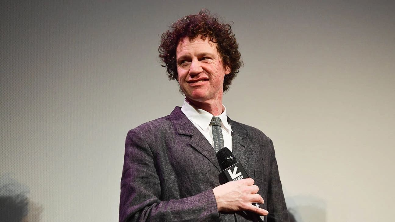 A photo of Chris Morris on stage with a micrphone, pulling a disgruntled expression.