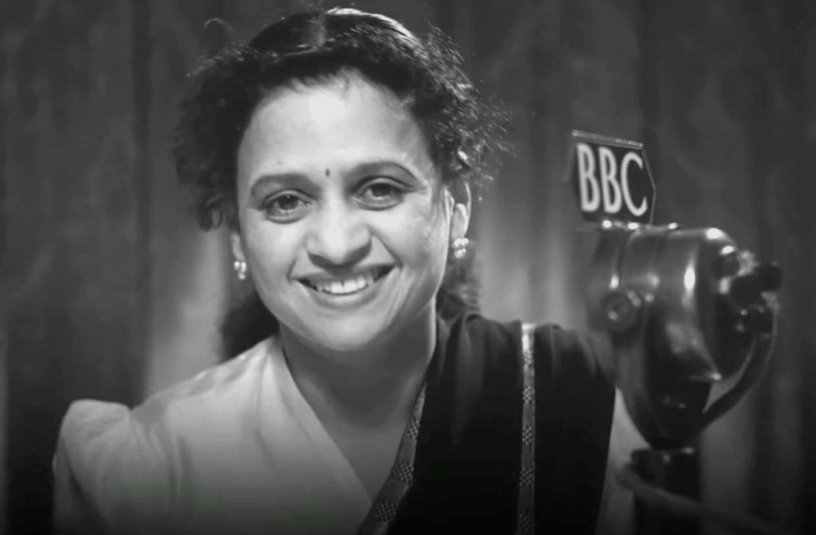 A black and white photo of Venu Chitale, behind the microphone in a BBC studio.