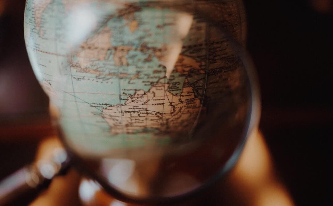 Image shows a magnifying glass being used to show Australia on a globe.