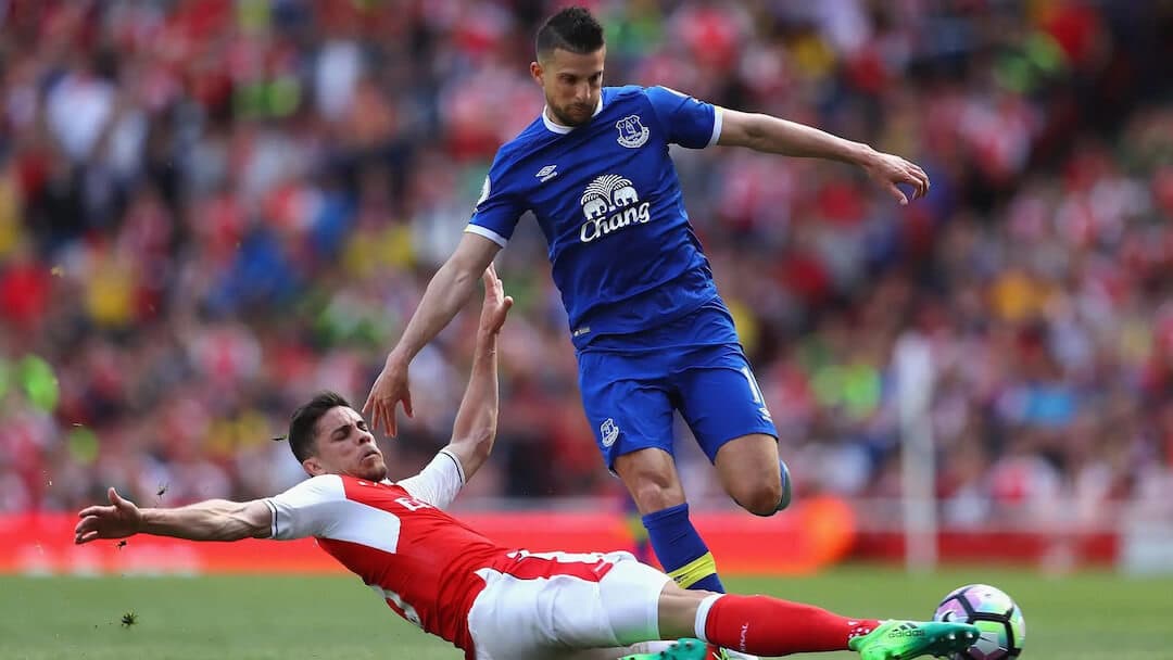 Image shows an Arsenal football player tackling an Everton player.