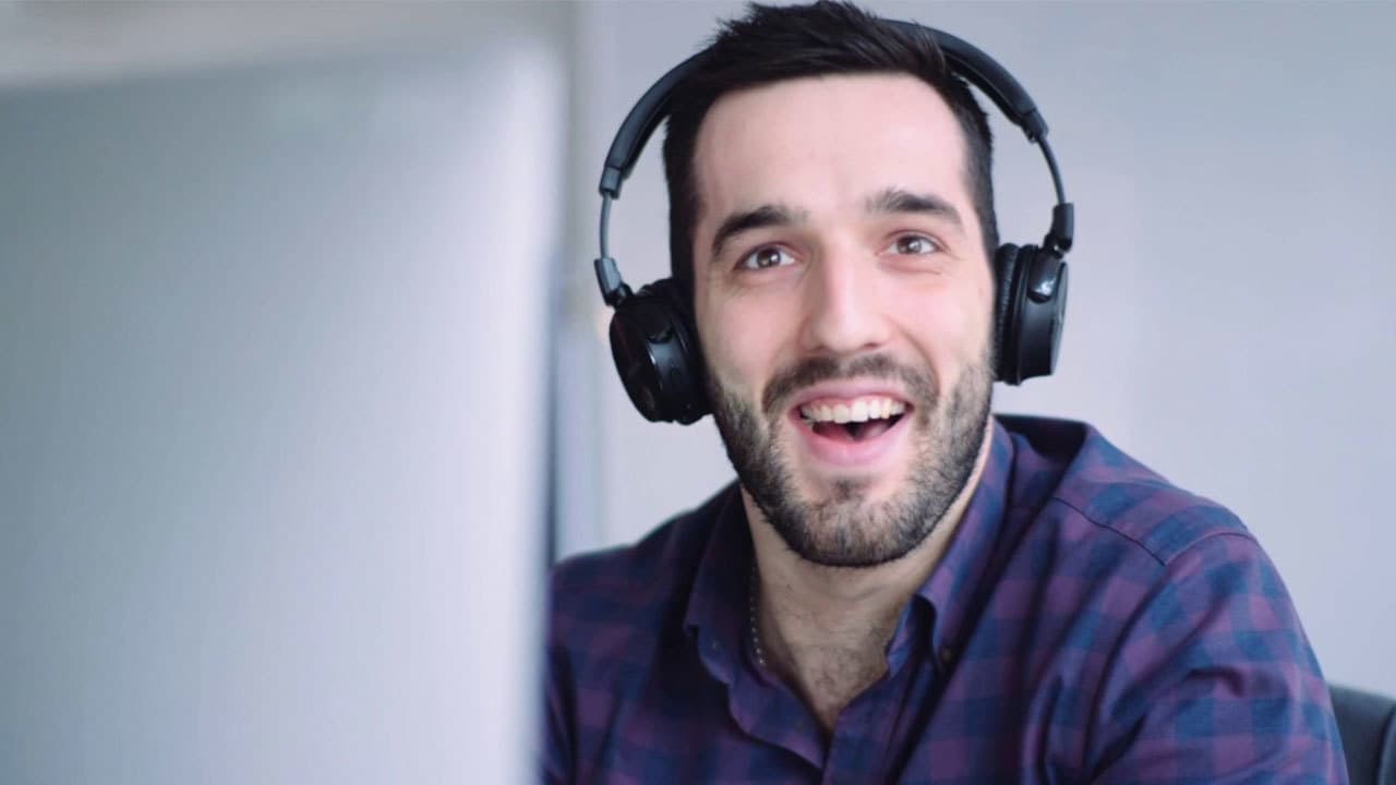 Image is of a man from the Radio.co team, smiling towards the camera whilst working on a computer and wearing headphones.