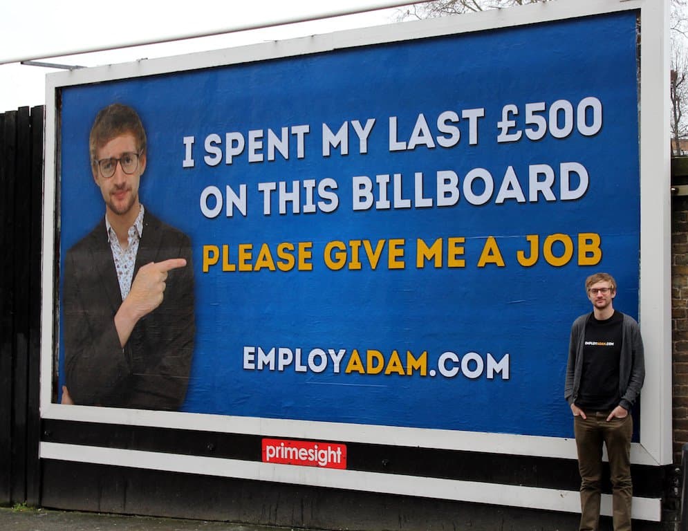Image shows Adam Pacitti standing next to his billboard advert.