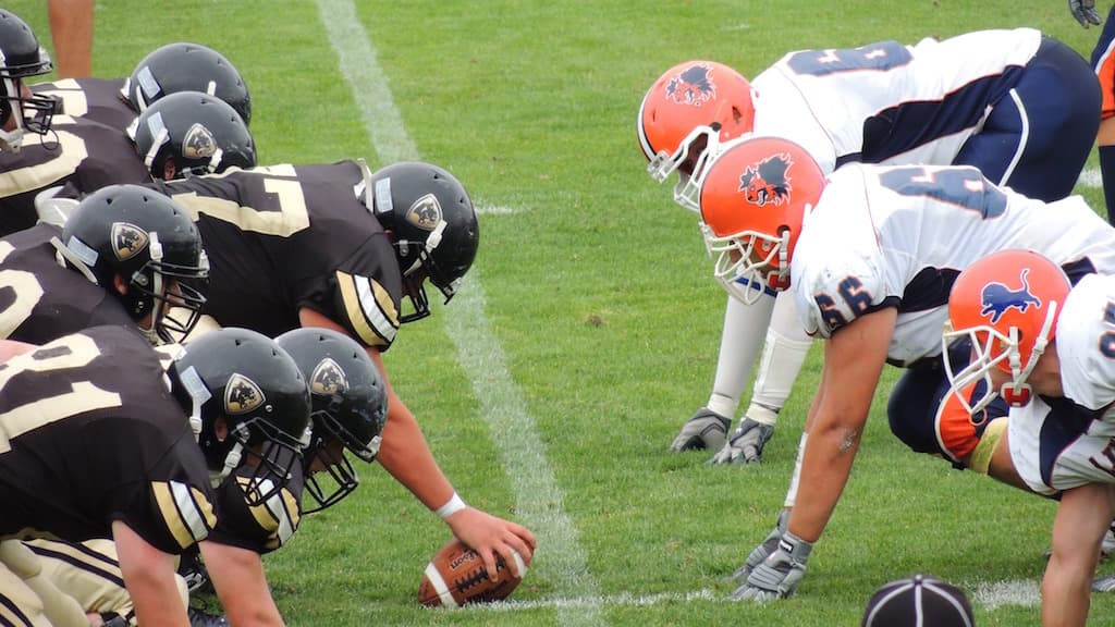 Two American Football teams crouch down by a football, during a down.