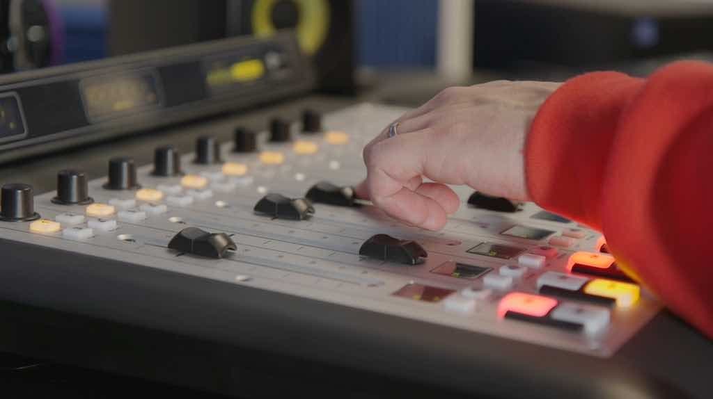 This is a grey Axia iQ AoIP Mixing Console Pro Studio with a white hand working on it.