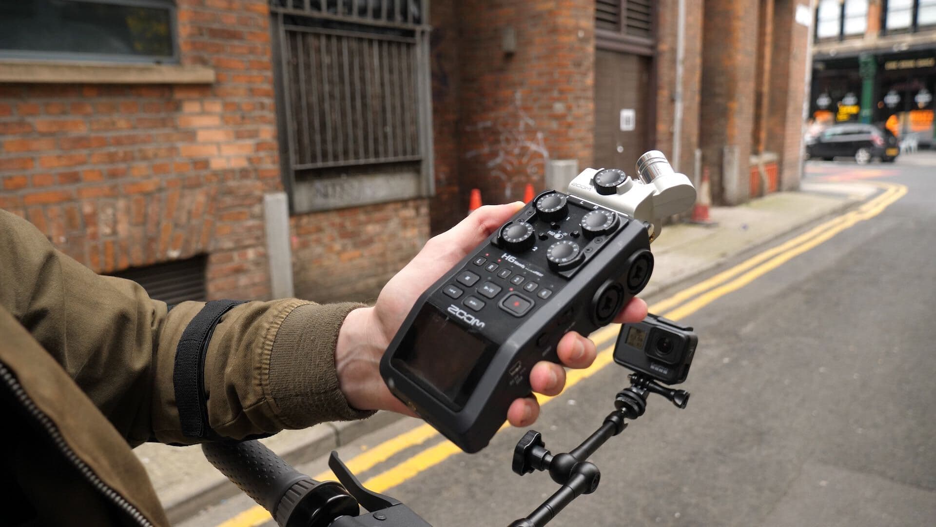 Image shows someone on a street holding a Zoom H6 interface above their bike.