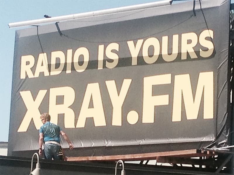 Image shows a man pasting some billboard artwork that reads
