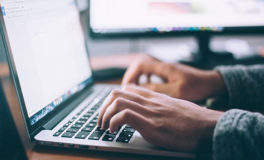 This is an image of a pair of hands typing on a Macbook keyboard. The person is wearing blue sleeves.