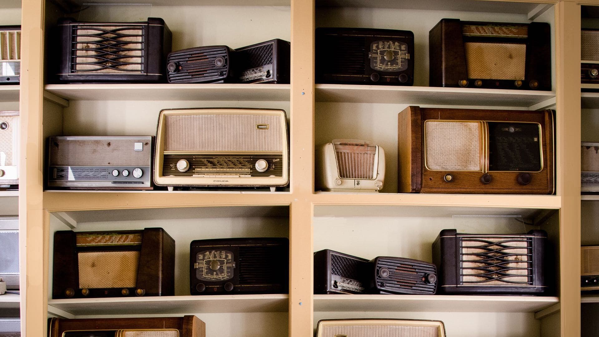 Image shows multiple old-fashioned radio sets on some shelves.