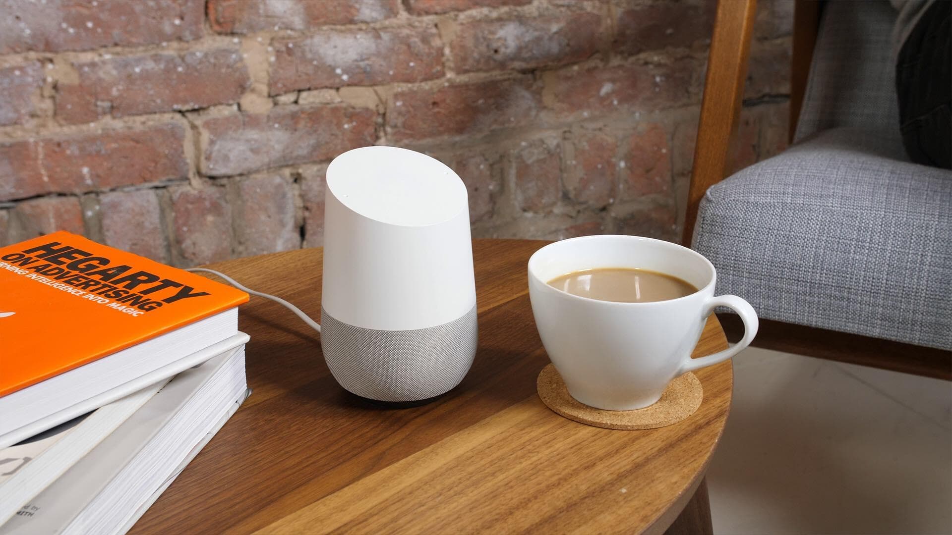 Image shows a coffee table with a cup of coffee, smart speaker and a pile of books on it.
