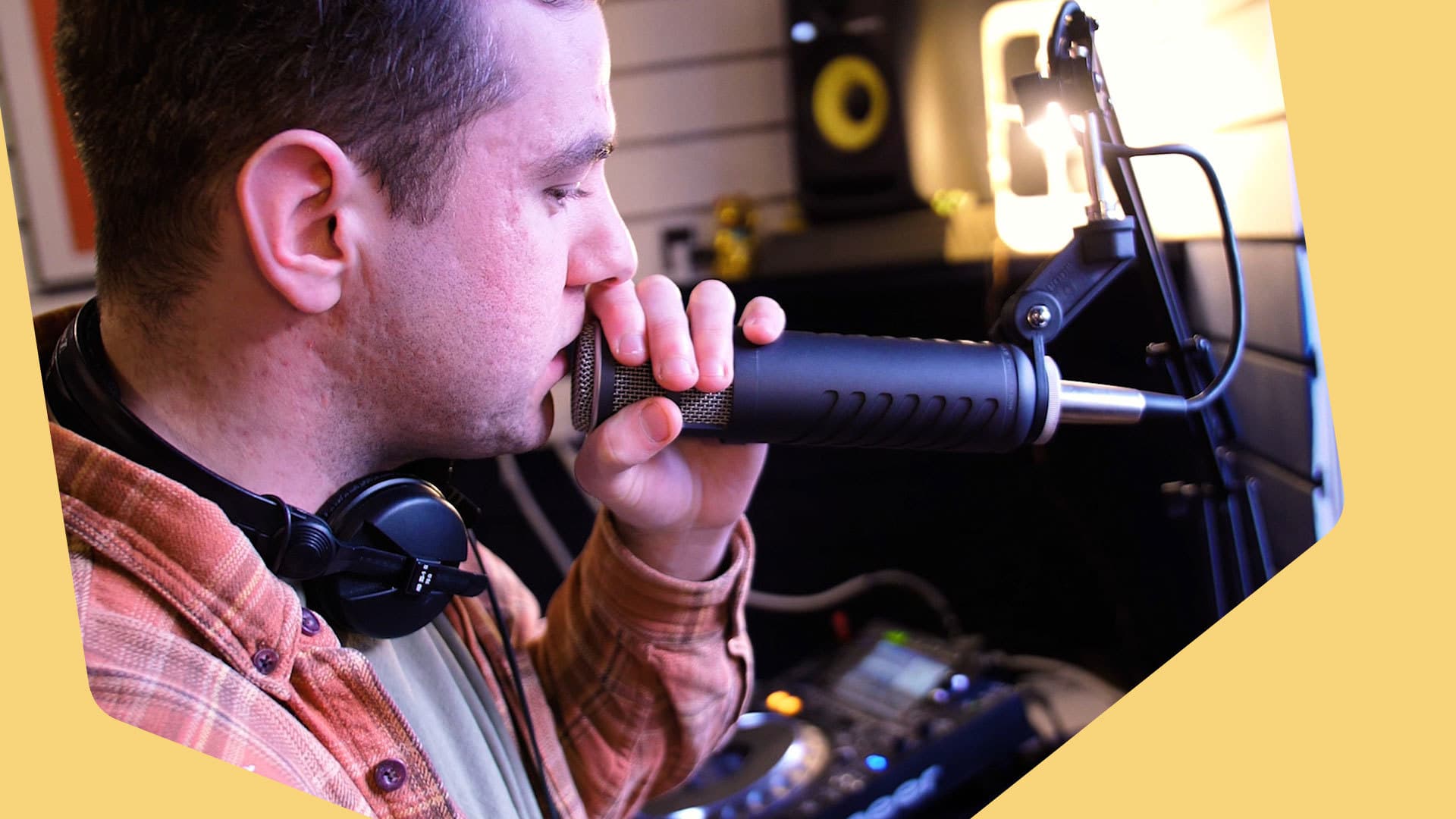 This is a radio presenter with his mouth very close to the microphone on a stand. He is a white man with black hair wearing a checked plaid top.