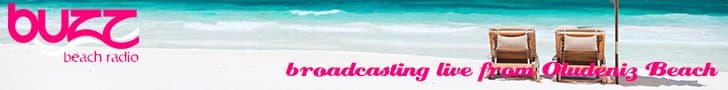 This is another stock banner image for Buzz Beach Radio's logo - the words in pink on a beach with two loungers visible from behind. Beneath it in pink reads "broadcasting live from Oludeniz Beach"