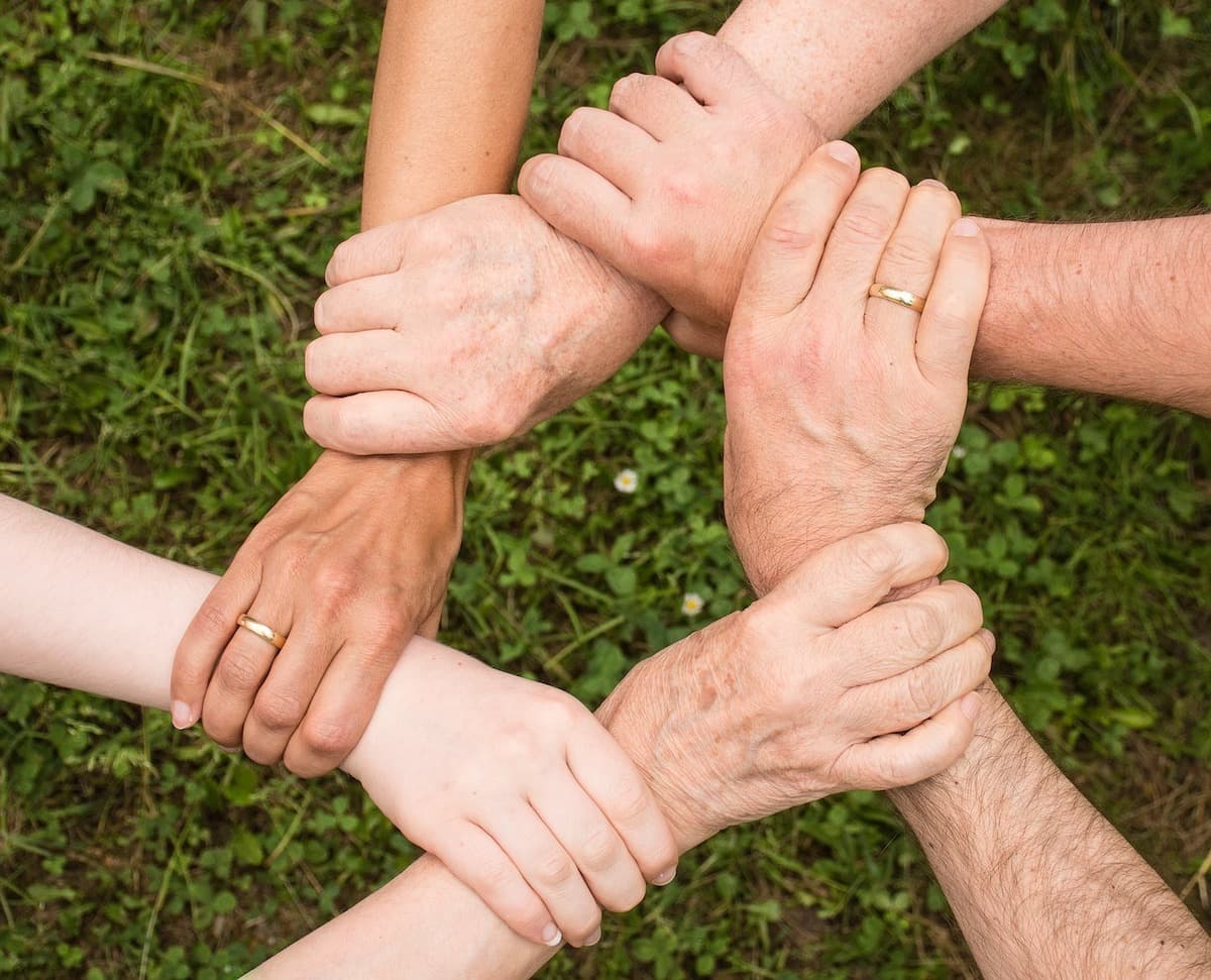Image shows 6 people's hands holding another persons wrist to make a circular shape.