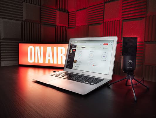 Image shows a laptop, microphone and a lit-up 'on air' sign on a desk.