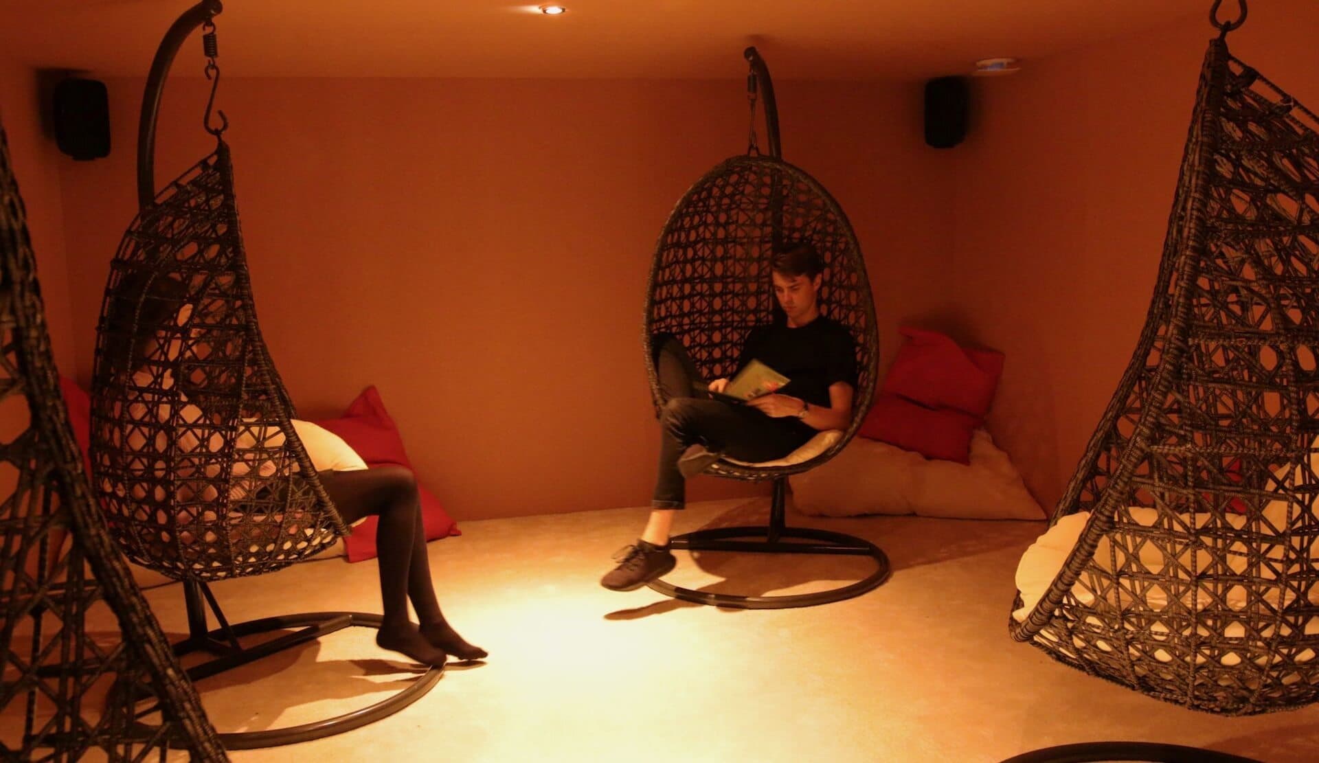 Image shows the Barbican Soundhouse shared listening space. It's a warm orange room with three egg chairs hanging from the ceilings and speakers in each corner.e