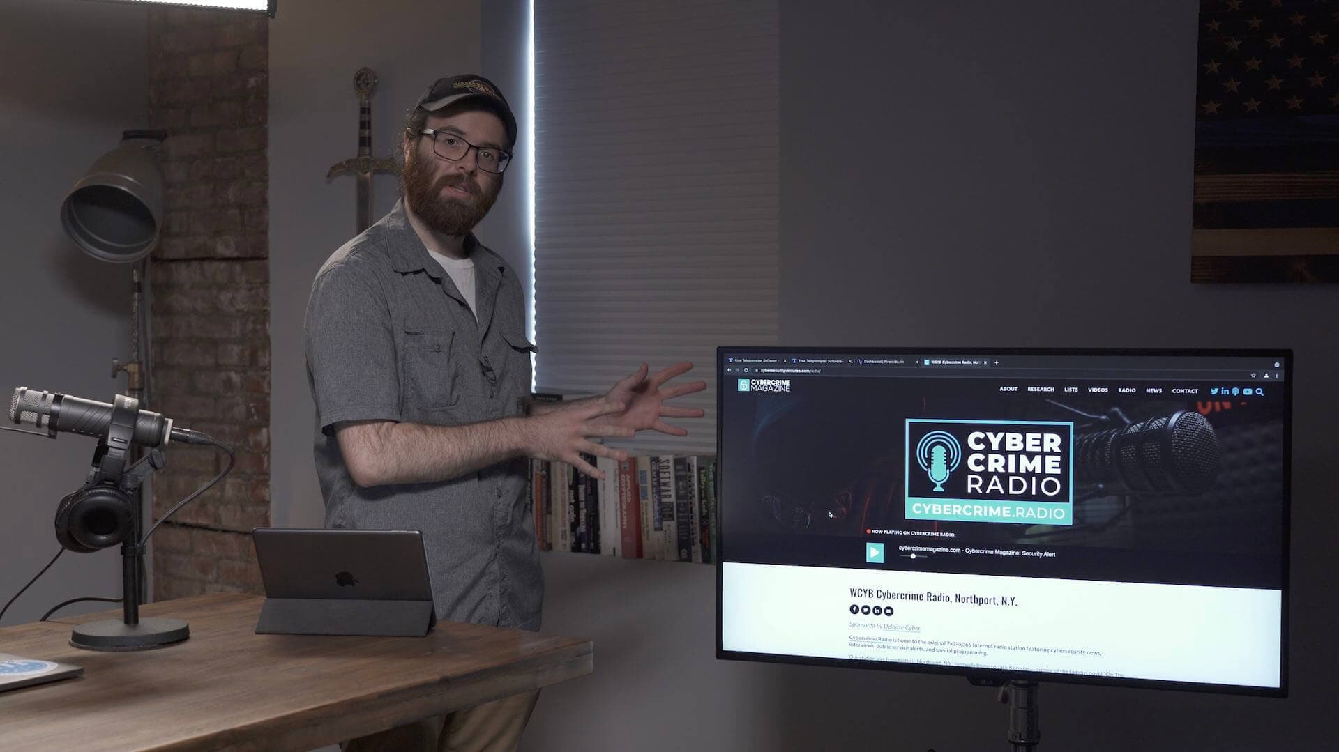 Image shows a man in the Cybercrime radio studio, and a computer which has the Cybercrime Radio website on the screen..