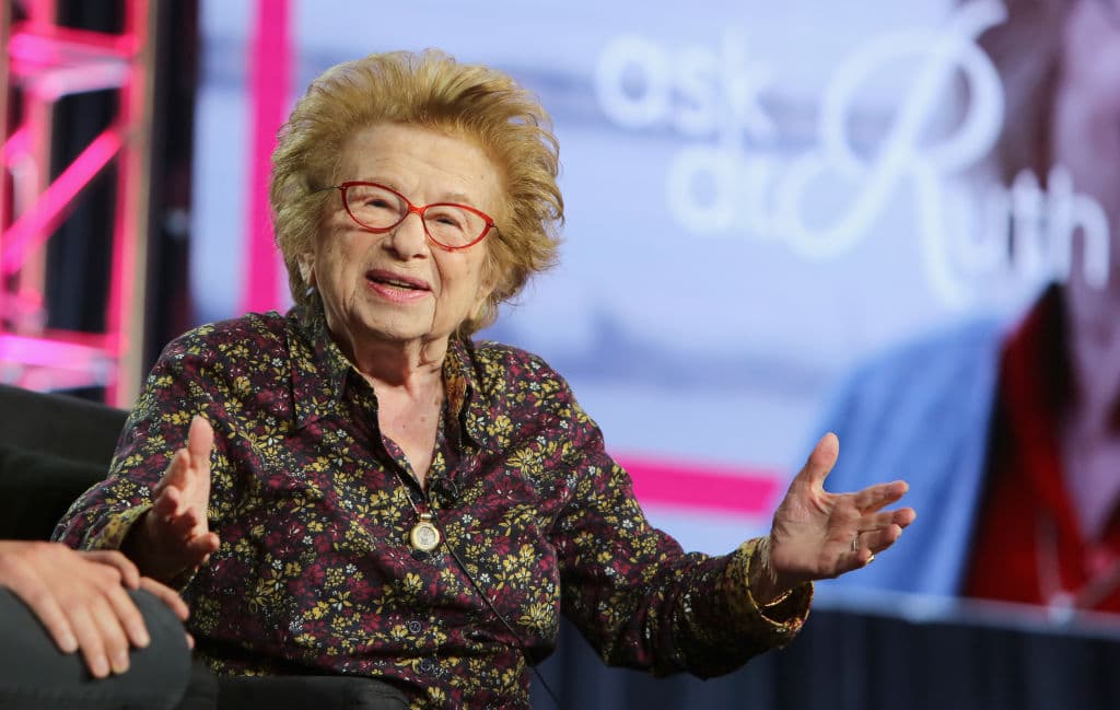 A photo of Dr Ruth Westheimer, sitting on a chair at a live event.