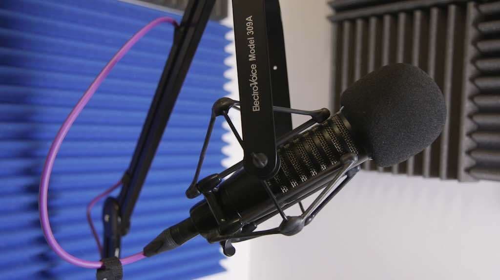 This is an image of the Electro Voice 309A Shock Mount with a black mic attached. The backdrop is a blue sound panel.