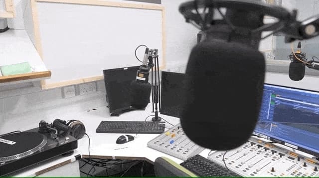 Image shows the inside of the Fuse FM radio booth, with a microphone in the foreground and the mixing desk and computer in the background.