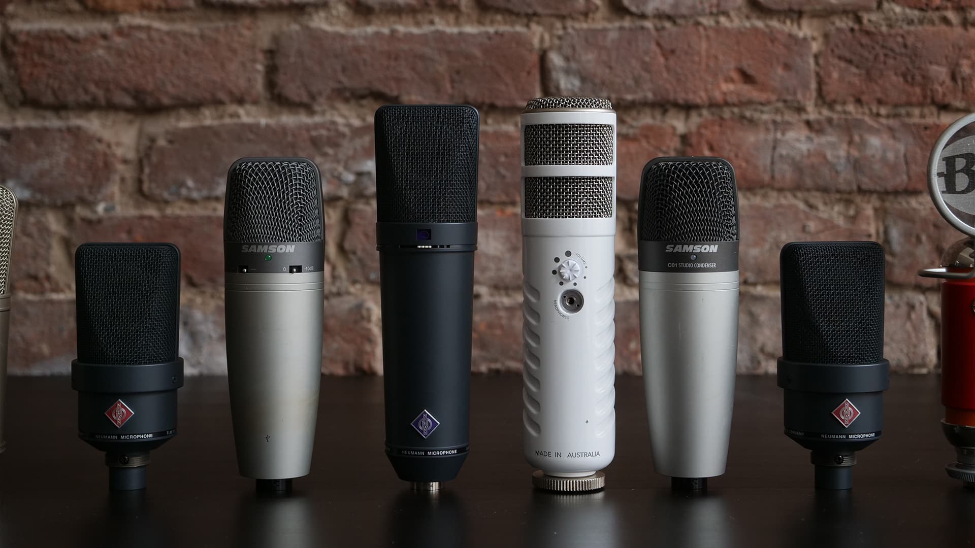 Image shows 6 different microphones stood upright and side-by-side on a desk.