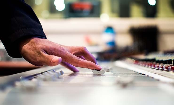 Image shows a close-up of a radio presenter putting a fader up on a mixing desk.