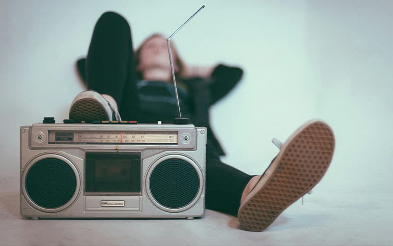 Image shows a woman lying down with one foot resting on a radio-set from the 80s.