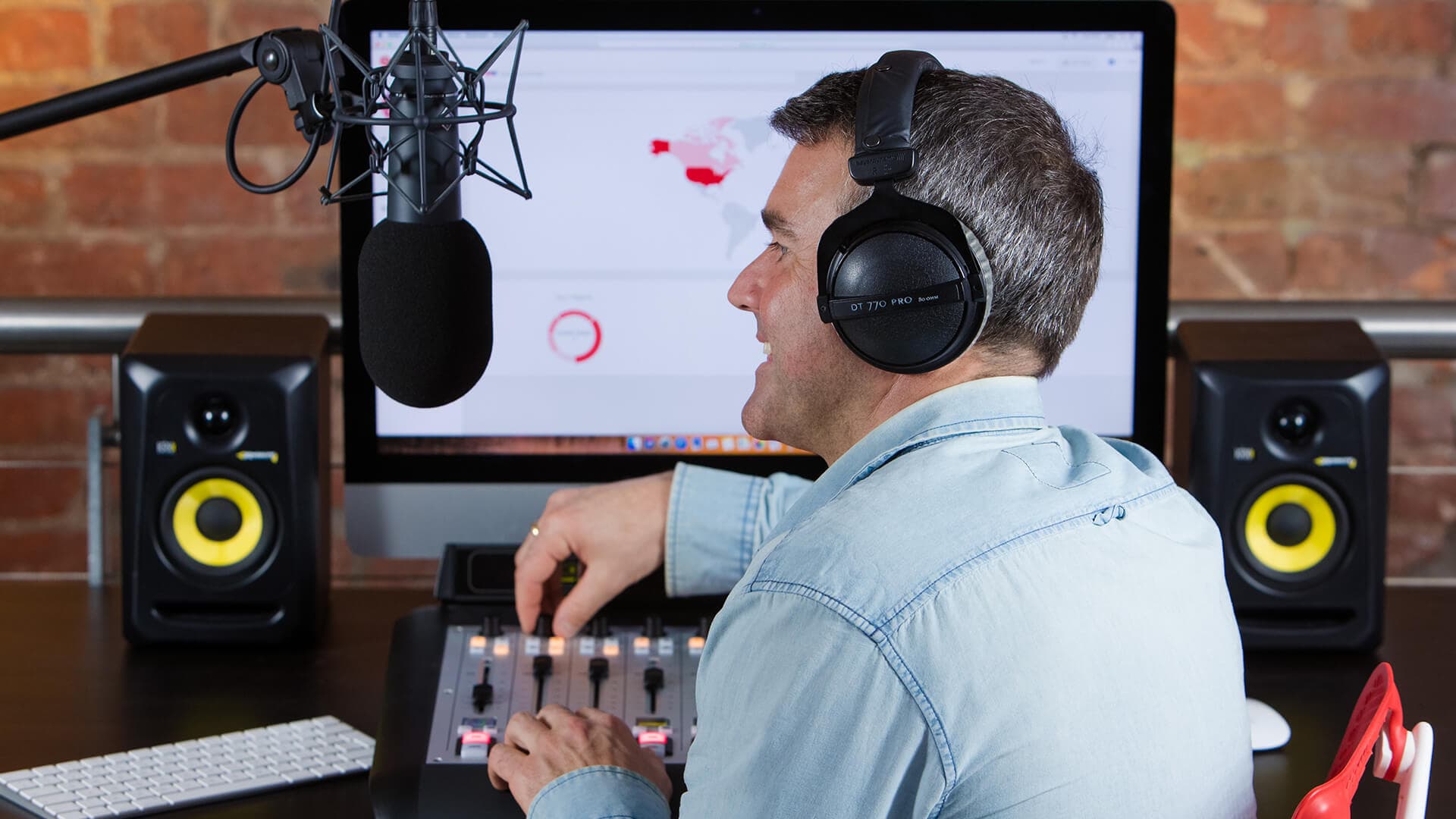 Image shows a man in a radio studio, speaking into a microphone and using the broadcasting desk.