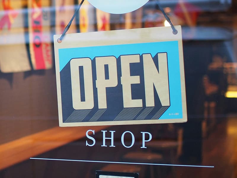 Image shows an 'Open' sign hanging in a shop doorway.