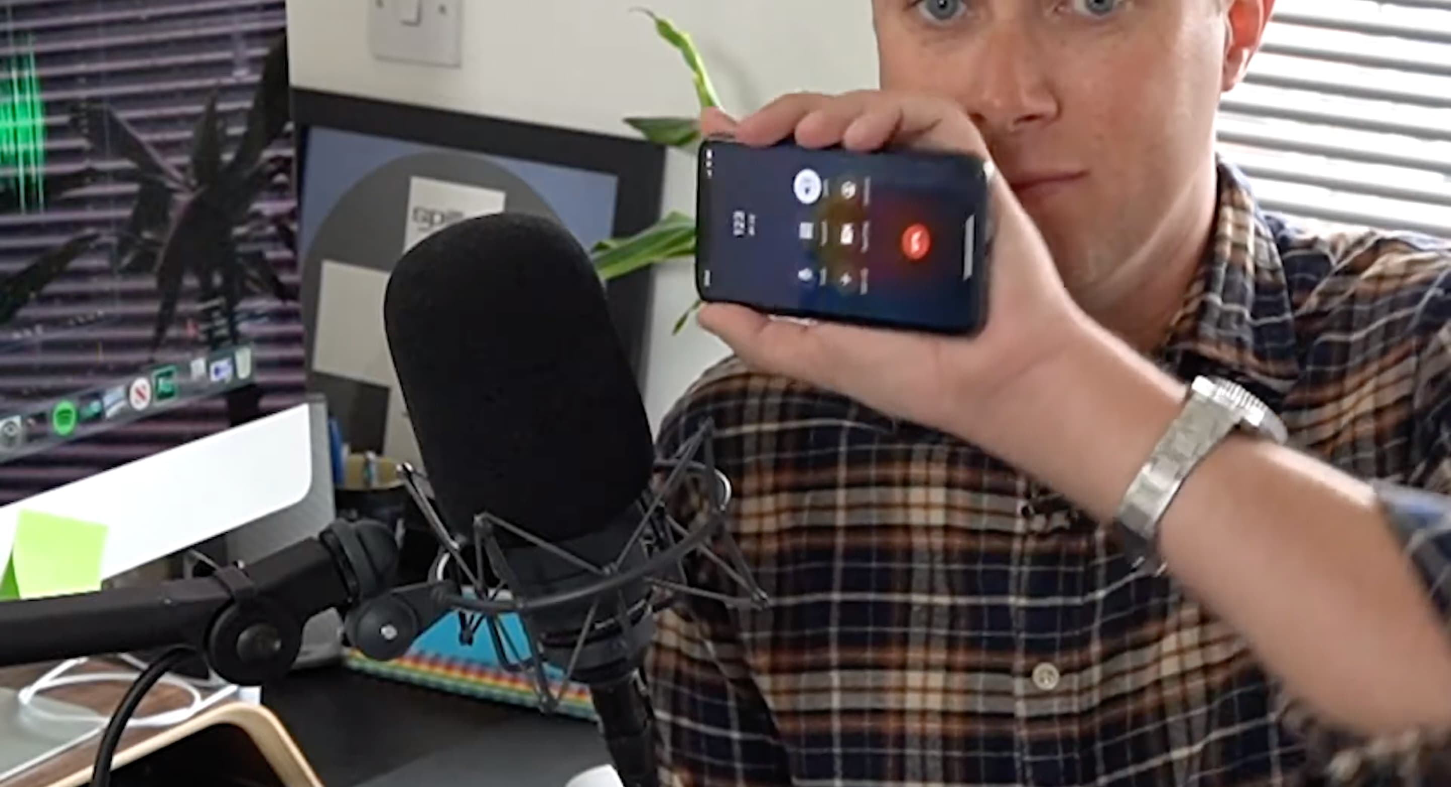 Image shows a man holding an iPhone - which is connected to a call, into a radio microphone.