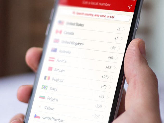 This is an image of a hand in the middle of the shot holding up an iPhone. On the iPhone screen is a list of countries and their corresponding area code. The backdrop is blurred.