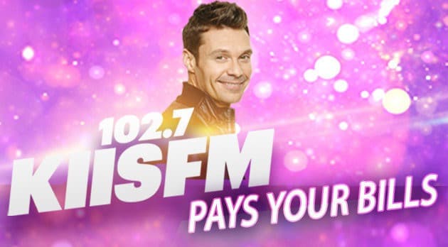 Image is the artwork campaign for KIISFM pays your bills. It features a purple, sparkly background with a presenter smiling at the camera and white font that reads "102.7 KIISFM PAYS YOURS BILLS"