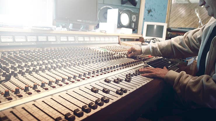 Image shows a man in a radio studio using a large broadcasting desk.