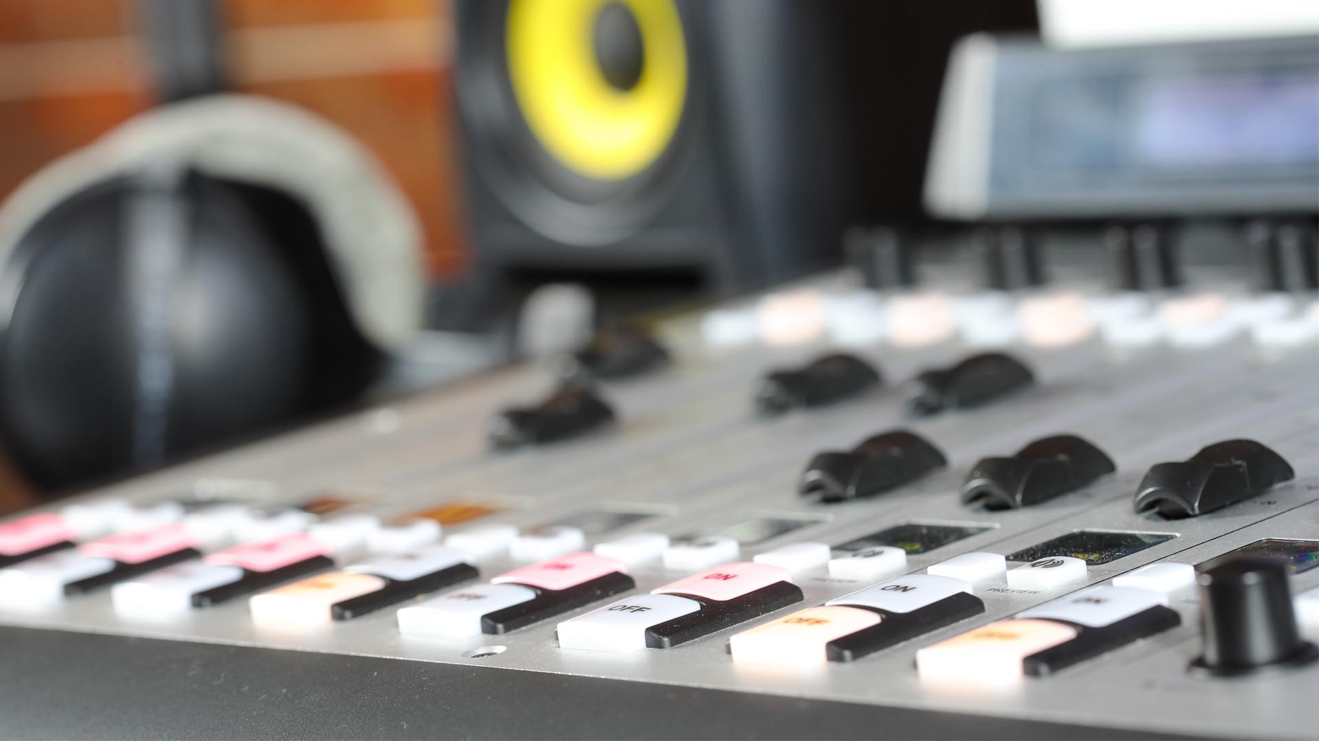 This is an image of a grey Mixer in the forefront of the image. In the back is a black and yellow speaker.