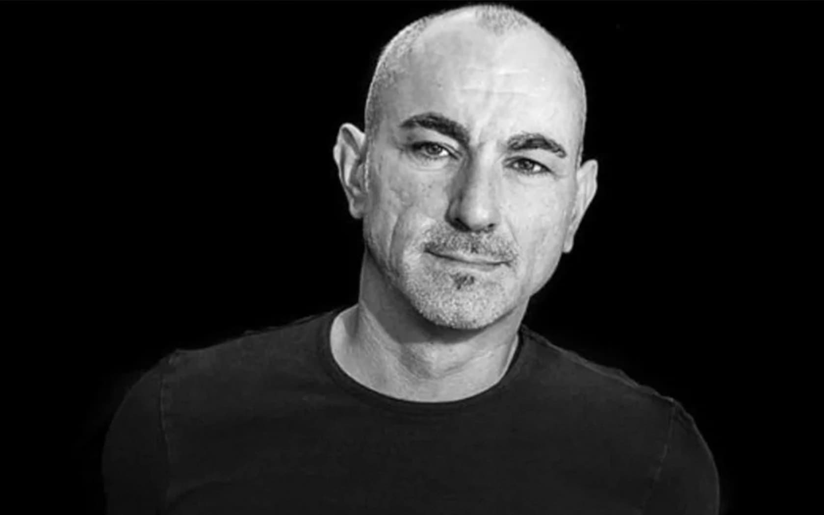 Image shows a black and white shot of the electronic composer, Robert Miles, looking at the camera and smiling.