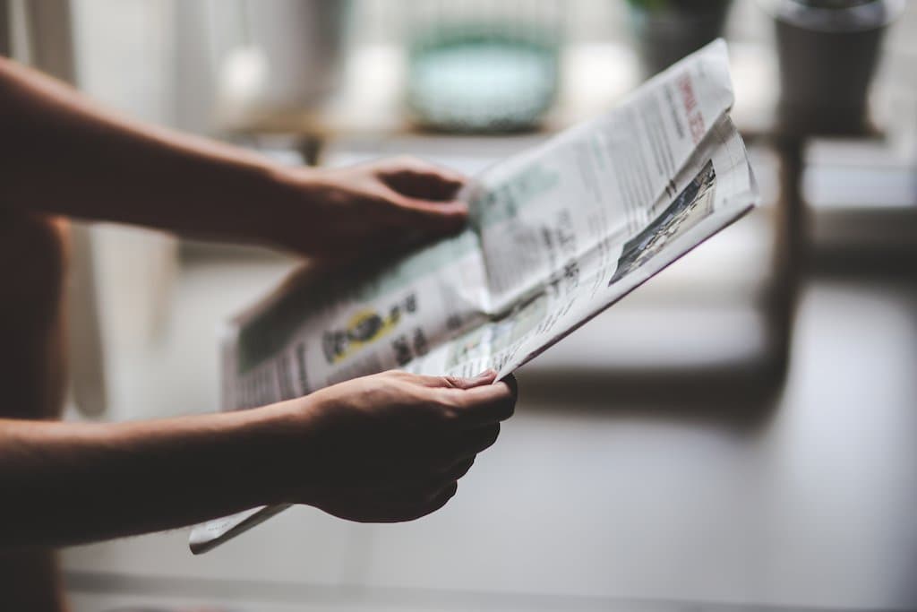 This is an image of a pair of hands holding a newspaper. There is one page. The background is neutral.