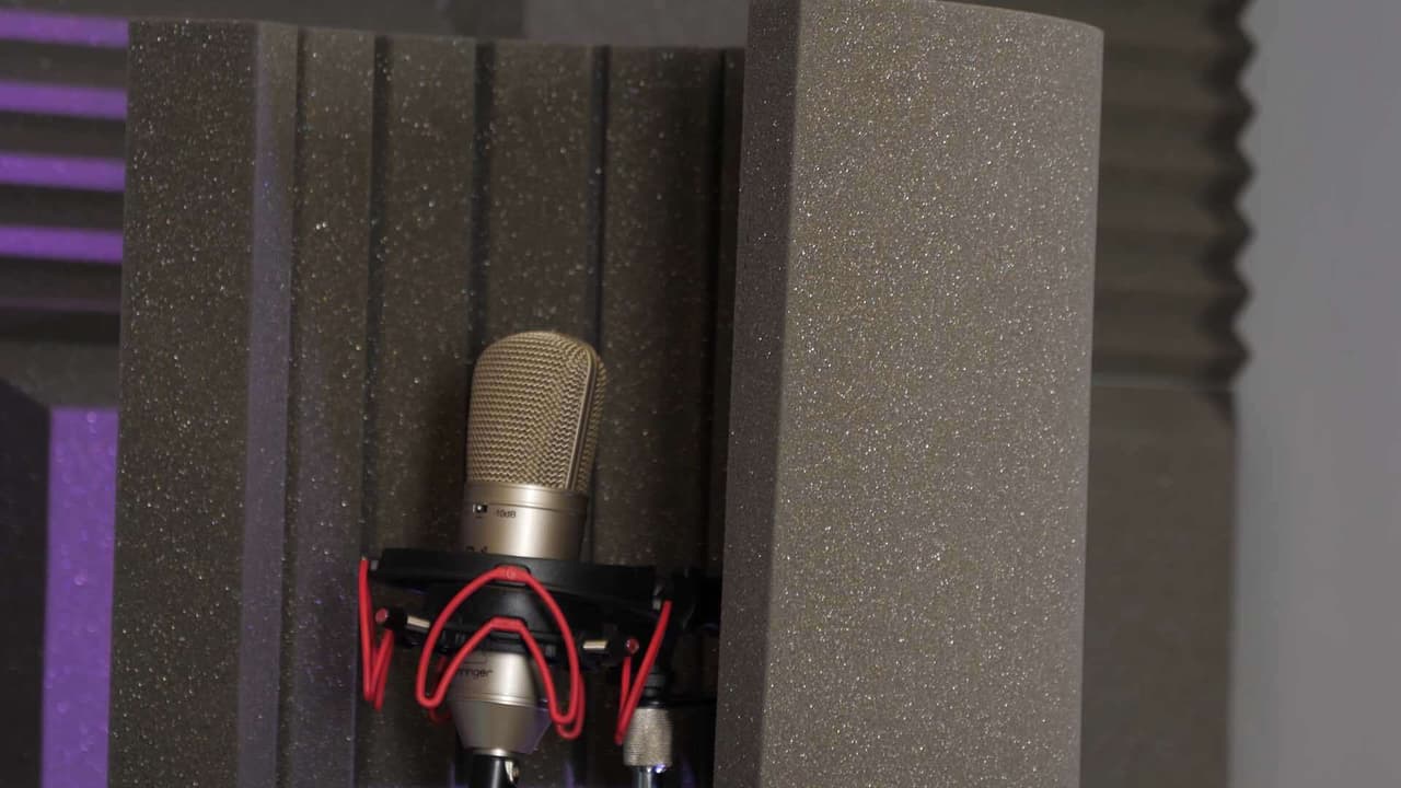 Image shows a microphone resting against some foam sound tiles.