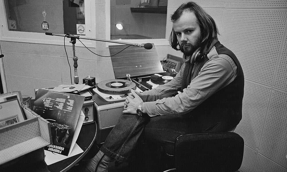 A black and white photo of a young John Peel in an old radio studio.