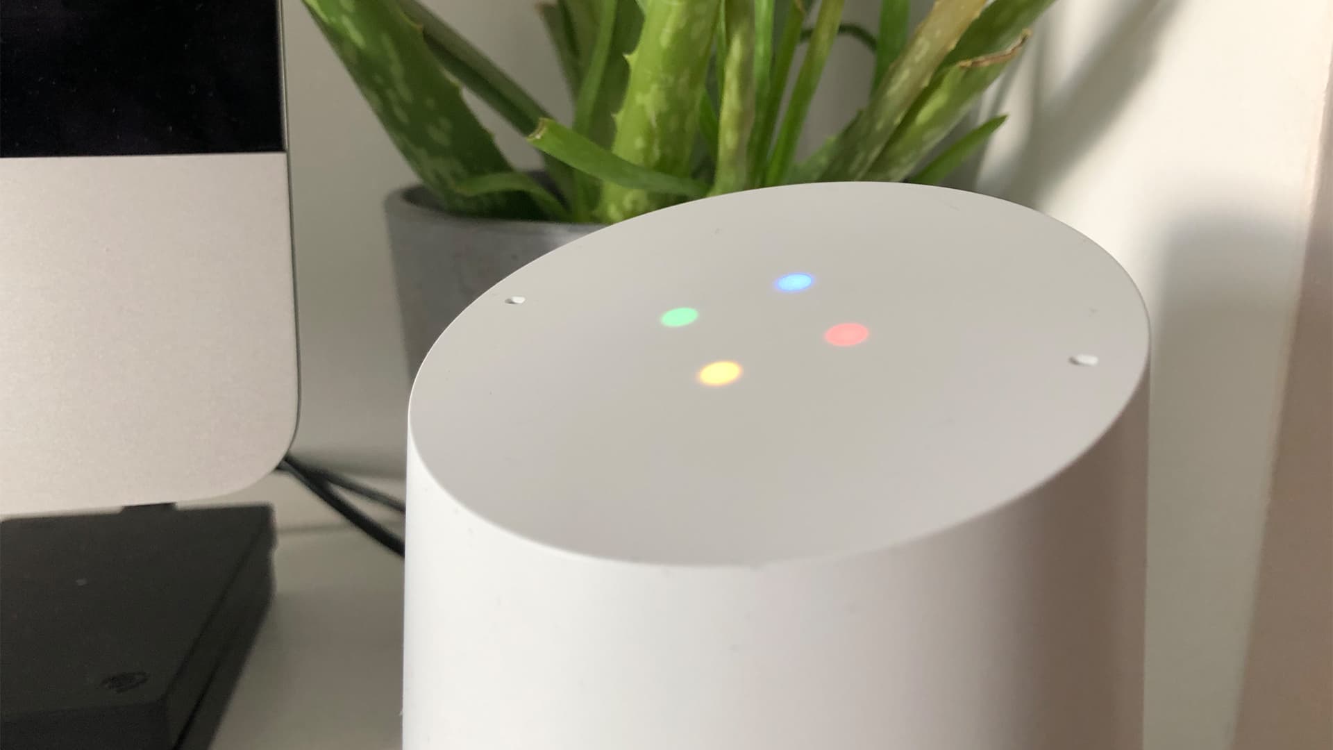 Image shows a close up of a Google Home smart speaker, with all 4 display lights on.