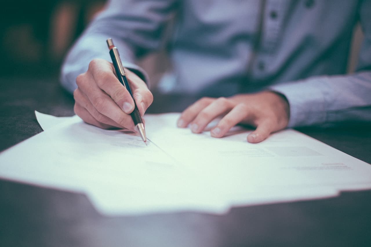 Image shows a man in a suit signing forms.