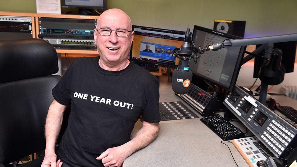 Image shows the British Broadcaster Ken Bruce inside a radio studio.
