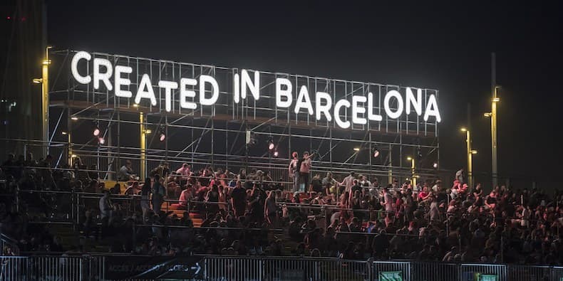 Image shows a stand of people at Primavera festival, above them is a lit up sign that reads "CREATED IN BARCELONA"