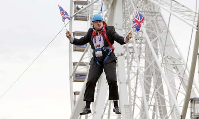 Image shows Boris Johnson suspended in the air by a zipwire and waving two Union Jacks.