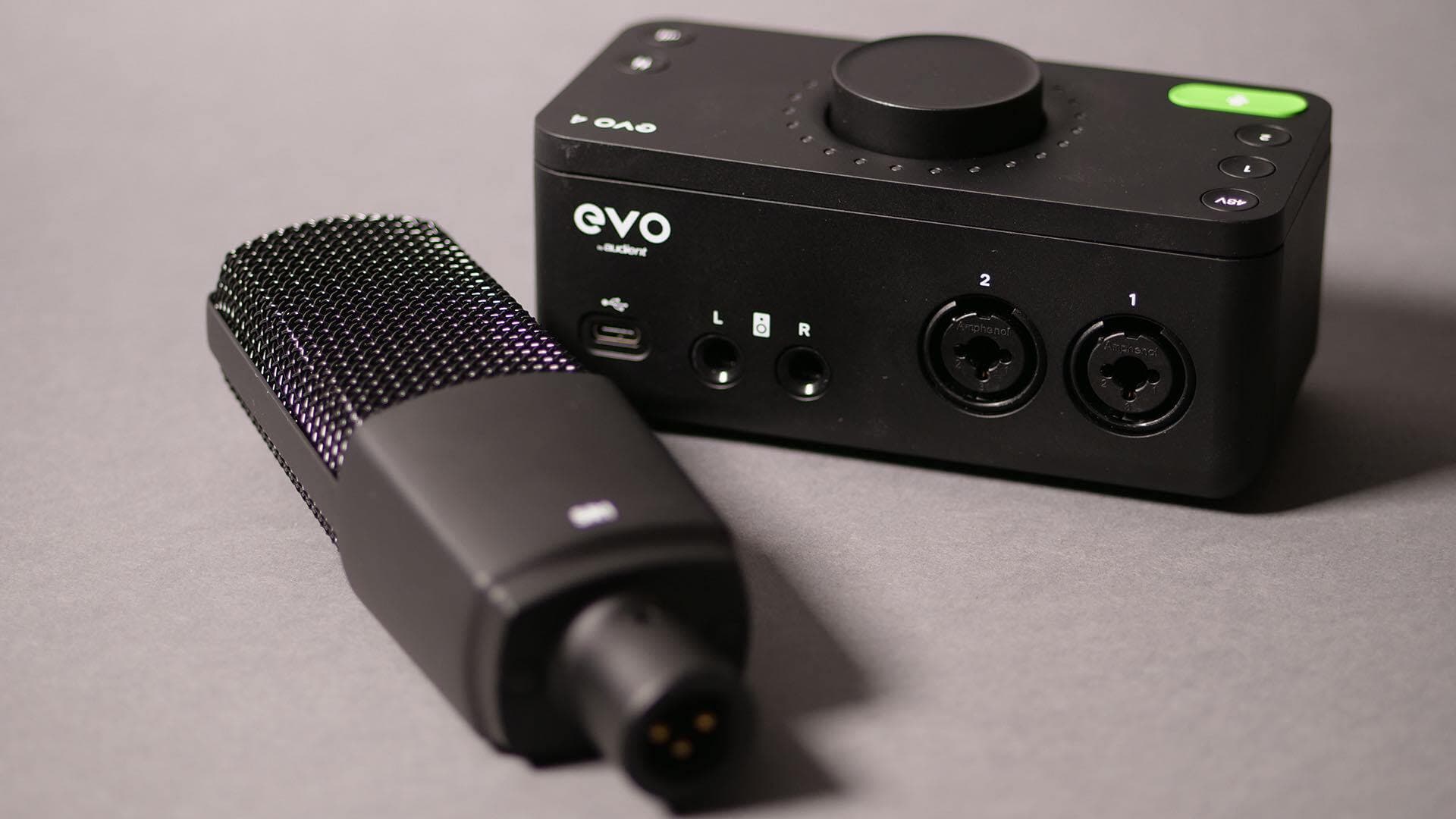 Image shows the Audient EVO SR1 microphone, on a table, next to the Audient EVO 4 interface.