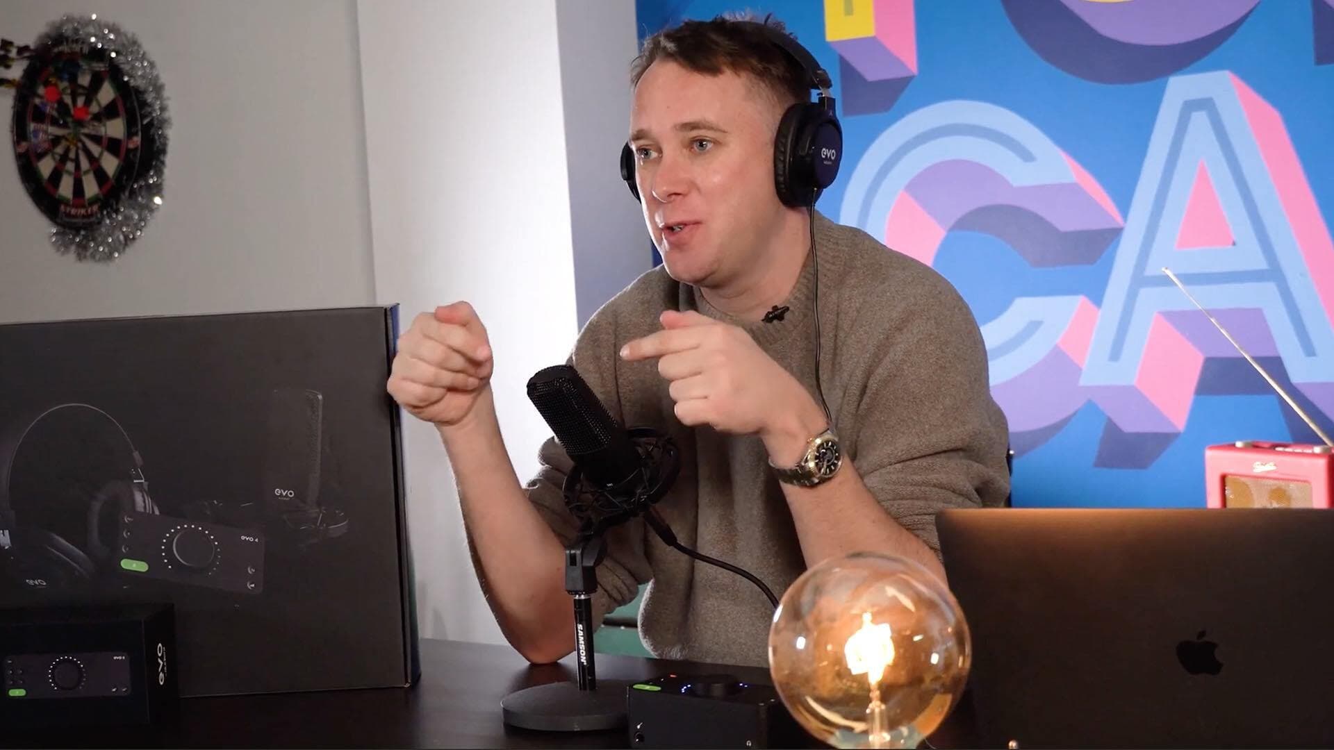 Image shows a man wearing the Audient EVO SR2000 headphones whilst sat at a laptop and speaking into a microphone..