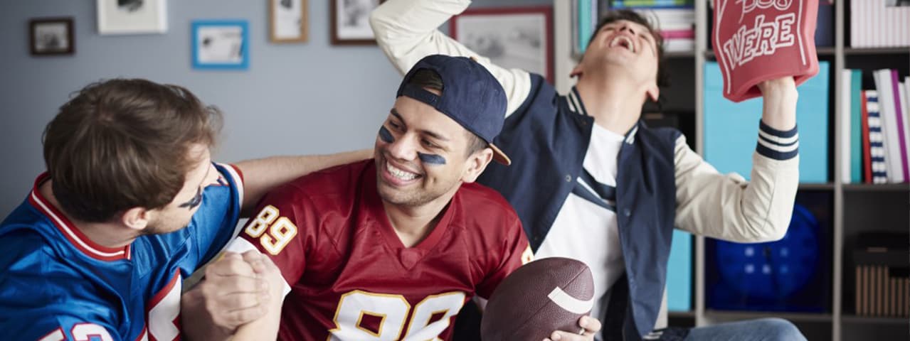 A group of American football fans celebrating in a college room.