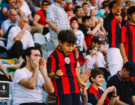 A close up of football fans in a stadium, with a young boy celebrating in the foreground.