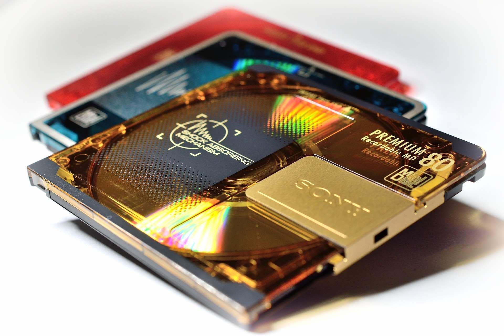 This is an image of three minidiscs. One is gold with rainbow accents and the other two are black and red. They are small squares with circular middles.