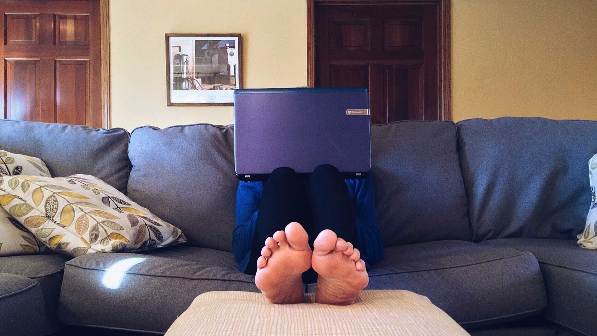 A person sitting on the sofa with a laptop with their feet up.