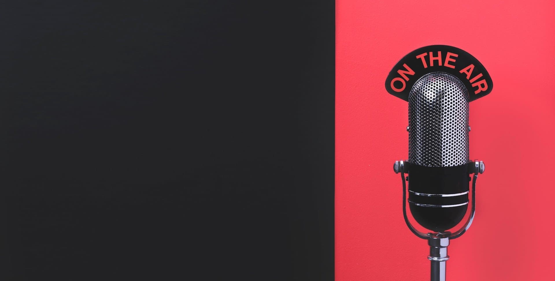 Image is a design featuring a rectangular shape which is black on the left side and red on the right. In the red section, there is an radio microphone and an 'On the air' sign perched on top of it.
