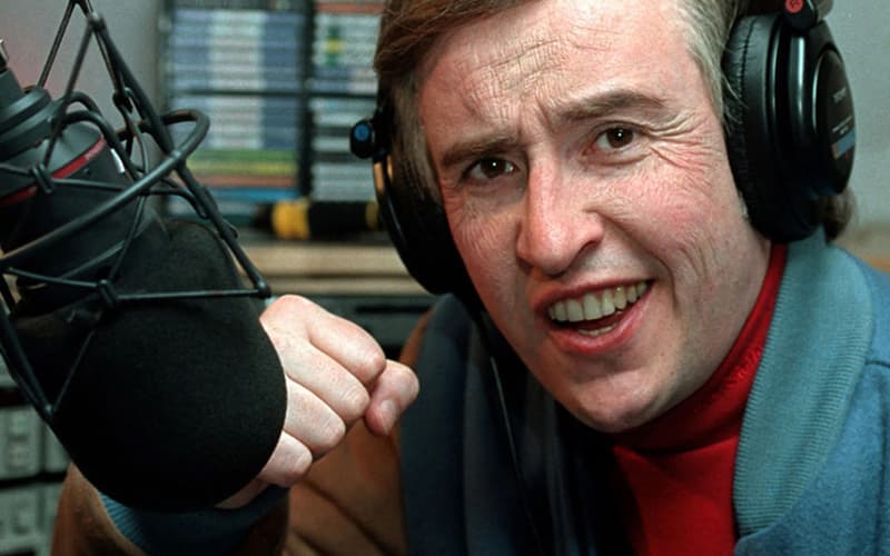 Image is a still of Alan Partridge in the radio studio, smiling at the microphone with his hand in a fist.