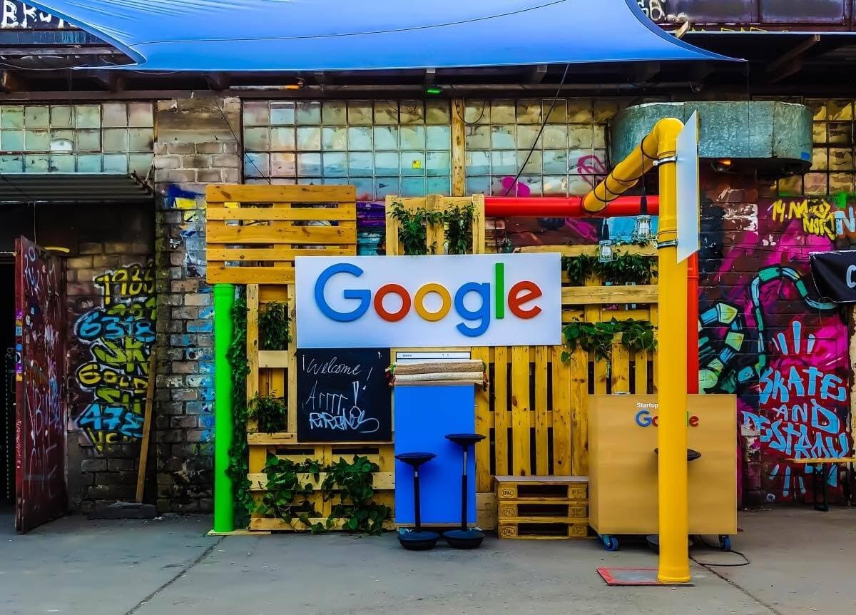 A street filled with graffiti and colourful street art is pictured. In the middle is a yellow chunk of art with the Google rainbow logo printed in the middle of the image.